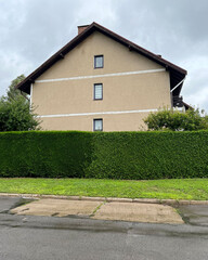beige two-story house with a green fence on a summer day after rain