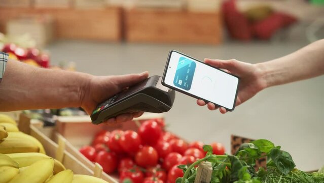 Digital Banking Concept: Shopper Using Mobile Phone with Contactless Payment Technology to Pay for Natural Goods at a Farmers Market. Street Vendor Holding an Electronic Online Payment Device