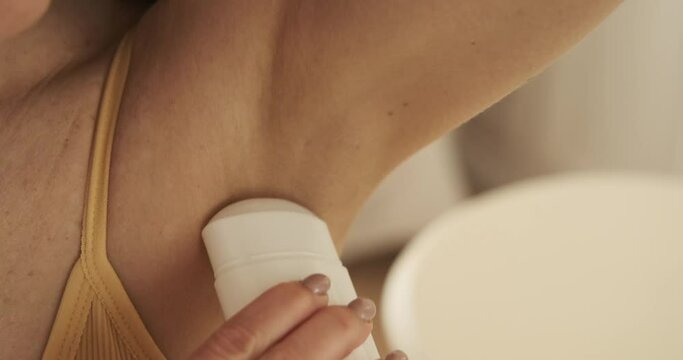 Extreme close-up shot, a woman is seen applying solid deodorant to her underarm with precision. The camera captures the smooth glide of the deodorant stick as it effortlessly coats her skin.