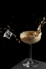 Long-stemmed cocktail glass, falling ice cube, frozen splashes stylish and captivating. dark background.