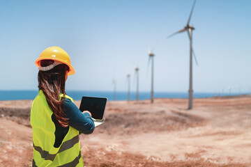 Female engineer working with computer tablet on wind alternative energy generator farm site - Industry and technology concept