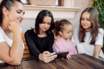 teenagers and one child having fun outdoors in a cafe. Friendship of children and teenagers. Four girls, dressed in different clothes, shout on the phone