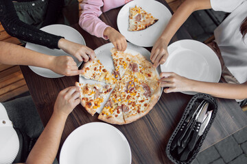 An overhead shot of a group of unidentified people grabbing a slice of Hawaiian pizza