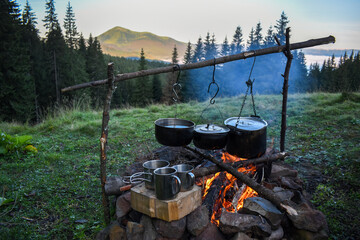 Sooty cauldrons on a fire in a tourist camp against the backdrop of a mountain and a spruce forest. Travel kitchen.