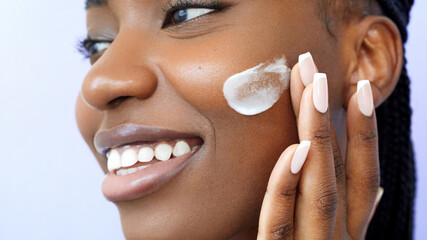Cream smear. Beauty and skincare. Skin hydration and oil balance. Portrait of African American young woman with afro braids hairstyle is applying cosmetic product on her face ans smiling