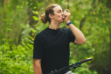 Asthma, fitness and man cyclist on a bicycle in a forest with breathing medical emergency during exercise or training. Outdoor, lung support and athlete with inhaler in nature for workout or wellness - obrazy, fototapety, plakaty