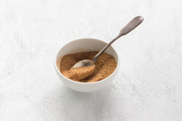 White bowl with a mixture of sugar and cinnamon for a delicious dessert on a light gray background, cooking stage