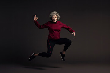 Fototapeta na wymiar A cheerful and confident grandmother dances in a dark studio in a casual outfit