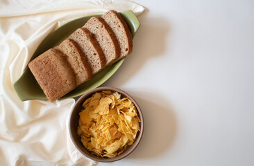 Brown bread slices and potato chips on a white background flat lay
