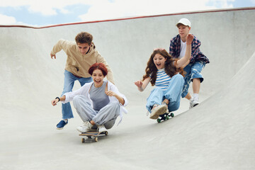 Group of cheerful friends, teens spending good time together on skatepark, skateboarding, laughing....