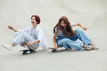 Laughing, cheerful, happy teen girls, friends in casual clothes having fun on skate park, sitting...