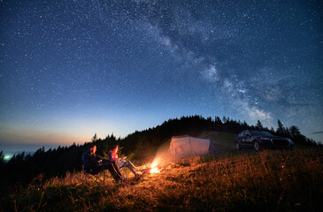 Night camping in the mountains under starry sky with Milky way. Travelling couple having a rest at...