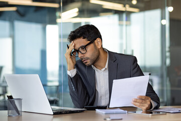 Serious thinking businessman at workplace, hispanic man upset thinking about financial reports,...