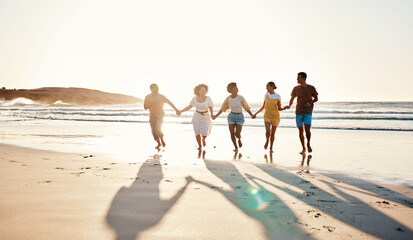 Friends, holding hands and running at sunset on beach in summer or walking together on holiday in California with freedom. Group, silhouette or vacation with connection or support in community