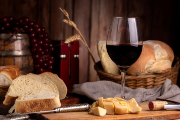 glass of red wine with bottle on table with homemade bread cheese wooden barrel with wooden boards