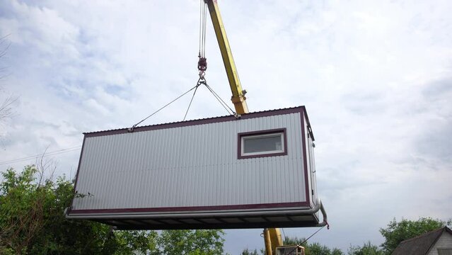 4k stock video of high tower crane operating transporting small wagon for temporary living in village isolated on blue cloudy sky background