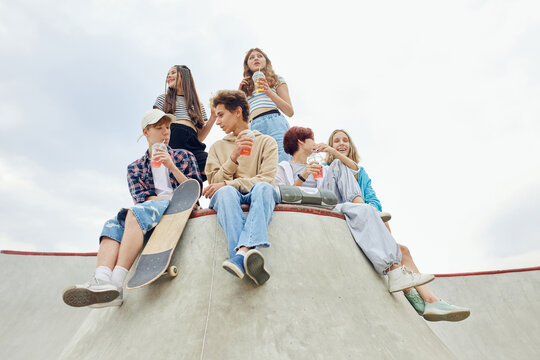 Cheerful, laughing, positive friends, teens sitting on skate park, ramp, talking, having fun and skateboarding. Youth culture, sport and dynamic, extreme, hobby and lesiure, friendship concept