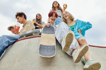 Summer chilling out. Friends, teenagers meeting on skatepark, drinking soda, talking, skateboarding...