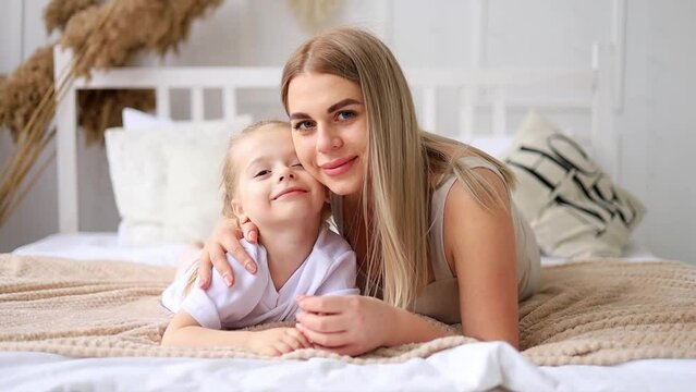 mom and daughter play, hug and kiss at home on the bed, lifestyle, tender relationship of a young mother and child, happy family and motherhood