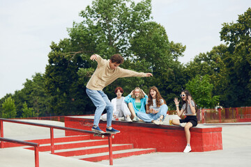 Naklejka premium Friends meeting on skate park, outdoors, skateboarding, training, having fun and talking. Summer activity. Concept of youth culture, sport, extreme, hobby and leisure, action and motion, friendship