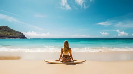 Zelfklevend Fotobehang  Une femme de dos sur la plage en train de faire une séance de méditation avant de faire du surf. En arrière-plan, de l'eau turquoise. © Gautierbzh