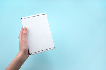 Obraz premium Female hands holding white package box on blue background.