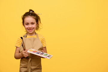 Beautiful kid girl with paint brush and watercolour palette, inspired little painter, artist smiles...