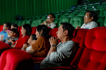 Wide shot of Asian man look scary or panic during watch movie with his family in cinema theater and...