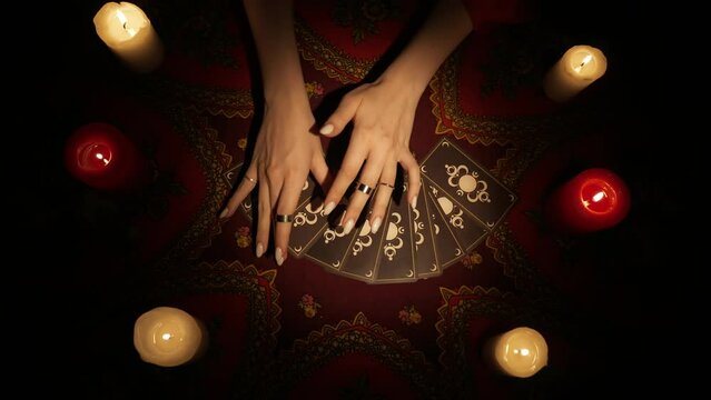 Top view, woman moving her hands over a fan of tarot cards and picks one card, opens it to the camera.