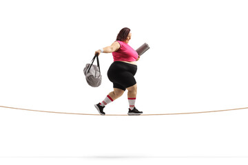 Side shot of an overweight woman with a sports bag and ezercise mat walking on a tightrope