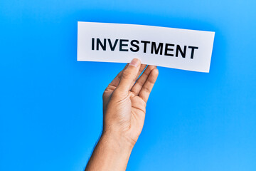 Hand of caucasian man holding paper with investment word over isolated blue background