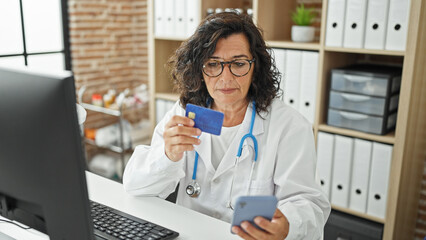 Middle age hispanic woman doctor shopping with smartphone and credit card at the clinic