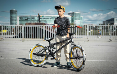 A boy in a cap and T-shirt rides a bmx bike and learns to perform tricks near a special ramp for...