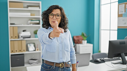 Middle age hispanic woman business worker smiling confident pointing with finger at the office