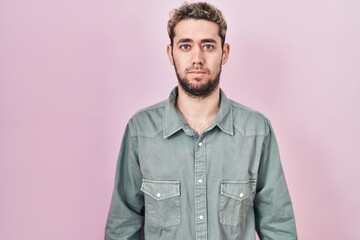 Hispanic man with beard standing over pink background relaxed with serious expression on face. simple and natural looking at the camera.