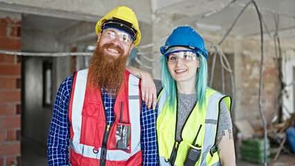 Man and woman builders smiling confident standing together at construction site
