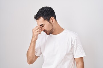 Handsome hispanic man standing over white background tired rubbing nose and eyes feeling fatigue and headache. stress and frustration concept.