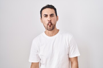 Obraz premium Handsome hispanic man standing over white background making fish face with lips, crazy and comical gesture. funny expression.