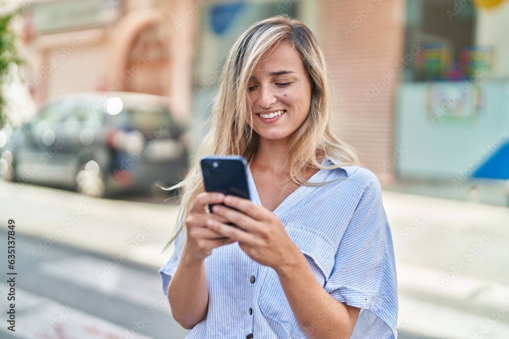 Sticker Young blonde woman smiling confident using smartphone at street