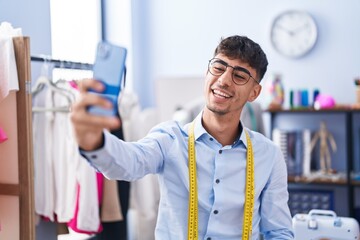 Young hispanic man tailor smiling confident make selfie by smartphone at tailor shop
