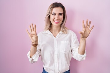 Young beautiful woman standing over pink background showing and pointing up with fingers number...