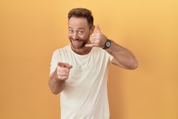Middle age man with beard standing over yellow background smiling doing talking on the telephone...