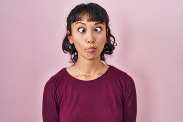 Young beautiful woman standing over pink background making fish face with lips, crazy and comical gesture. funny expression.