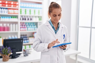 Young beautiful hispanic woman pharmacist using touchpad working at pharmacy