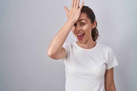 Beautiful Brunette Woman Standing Over Isolated Background Surprised With Hand On Head For Mistake, Remember Error. Forgot, Bad Memory Concept.