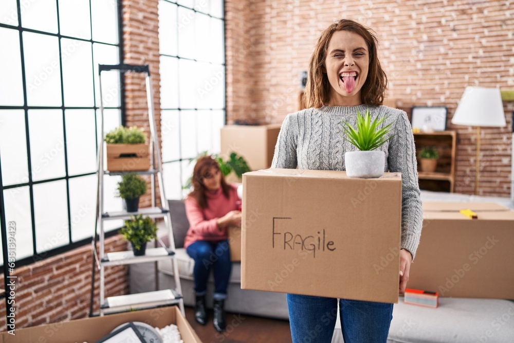 Sticker mother and daughter moving to a new home holding cardboard box sticking tongue out happy with funny 