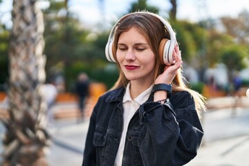 Young blonde woman listening to music smiling at park