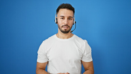 Young arab man business worker wearing headset speaking over isolated blue background