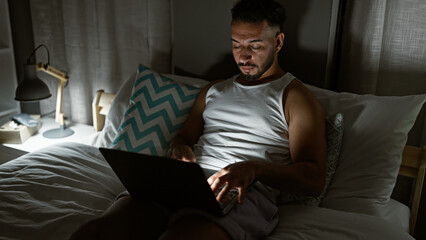 Young arab man using laptop sitting on the bed at bedroom