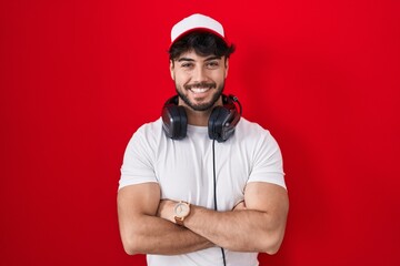 Hispanic man with beard wearing gamer hat and headphones happy face smiling with crossed arms looking at the camera. positive person.